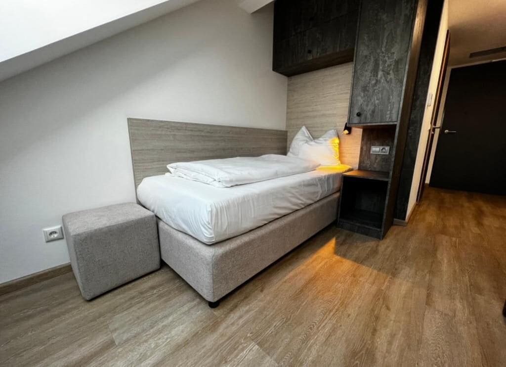 Quarto moderno com cama, mesa de cabeceira e um pequeno banquinho.