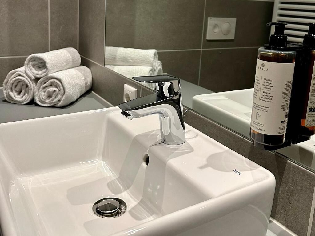 A modern bathroom with a white sink, chrome faucet, and a towel rack with neatly rolled towels.