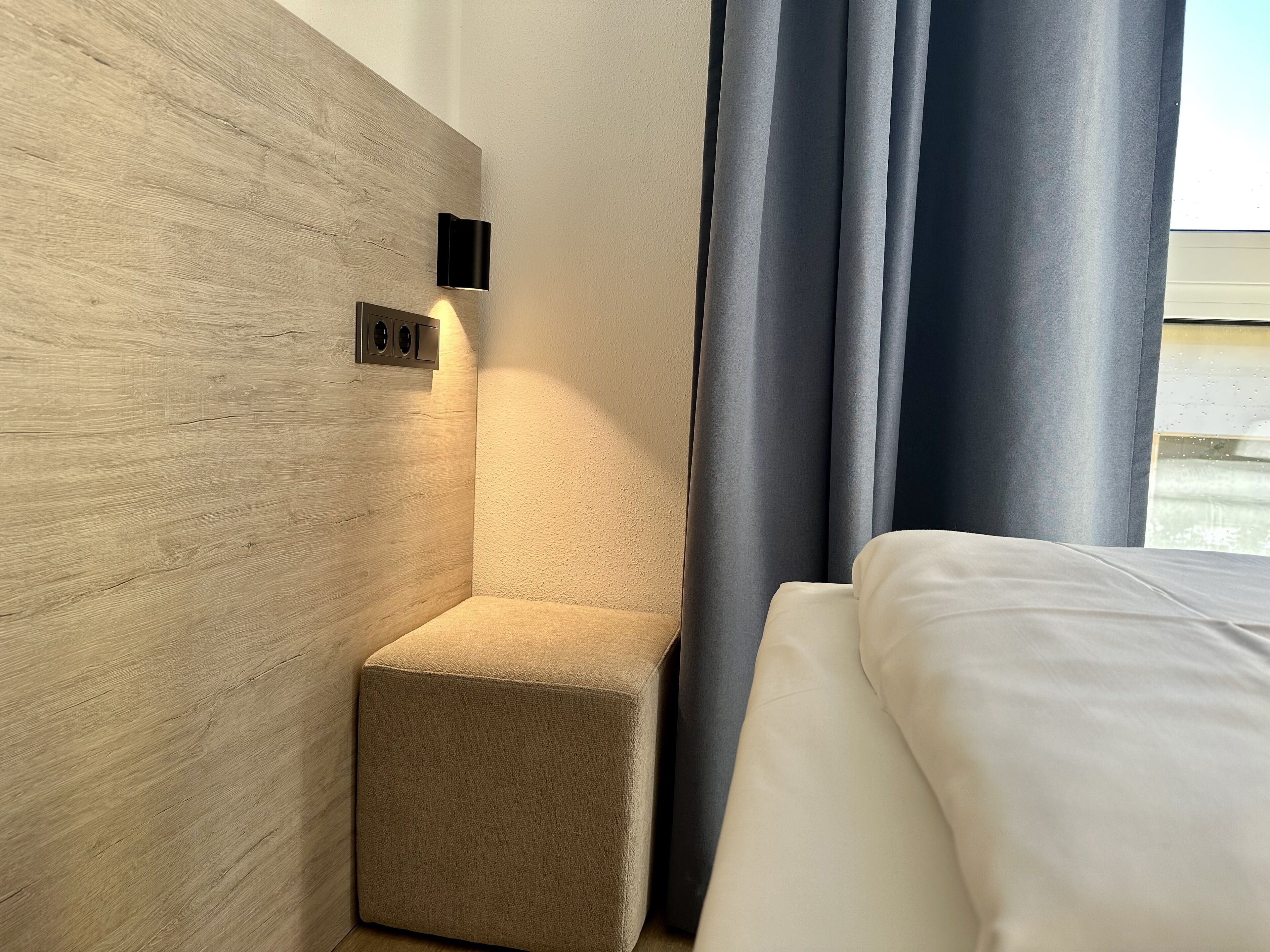 Ein modernes Hotelzimmer mit einem Holzkopfteil, einem kleinen Nachttisch und einem Bett mit weißer Bettwäsche.