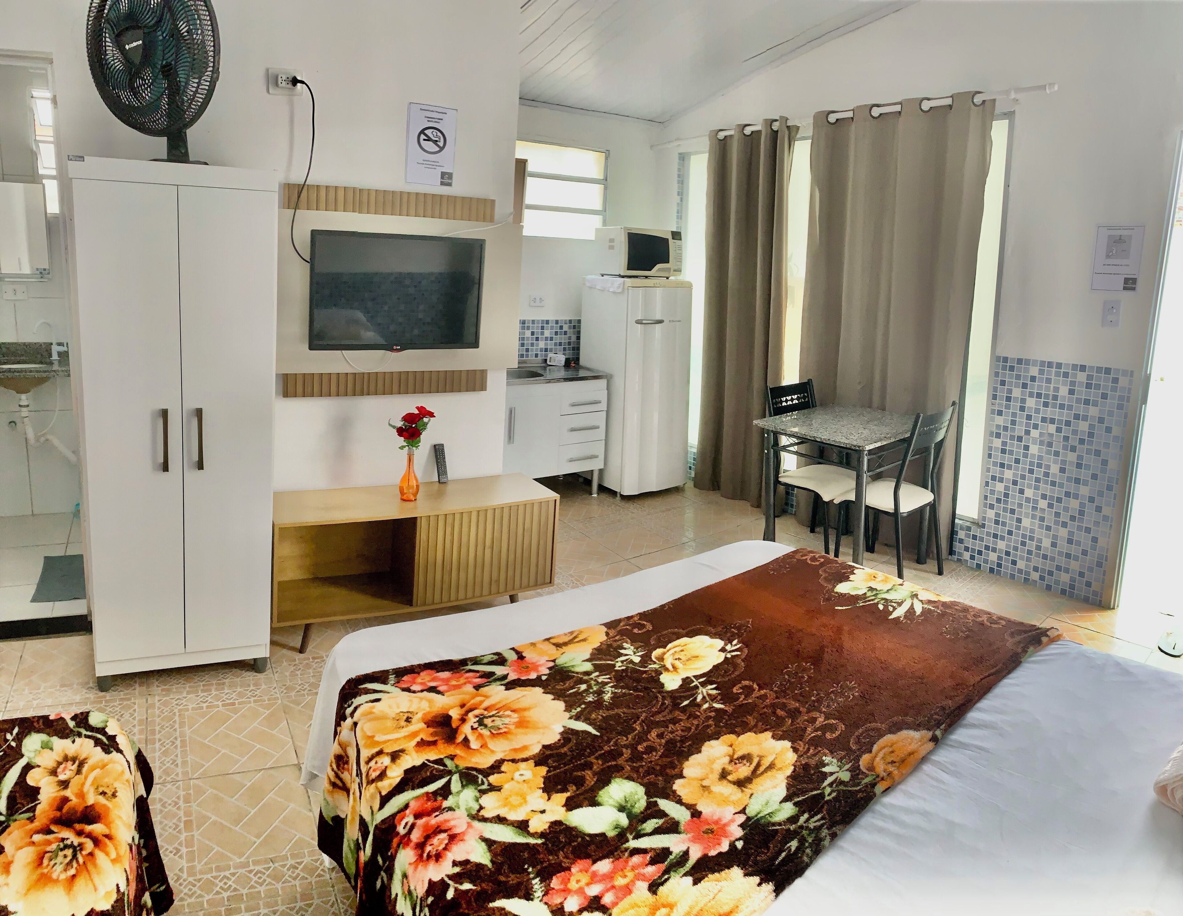A hotel room with a bed, a desk, a TV, a microwave, and a bathroom visible in the background.