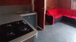 Une cuisine équipée d’une cuisinière, de placards et d’un mur en briques rouges. Le salon est agrémenté d’un canapé rouge.