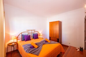 Une chambre à coucher avec un lit, une armoire en bois, une table de chevet, une lampe et une petite table sur laquelle se trouve une bougie.