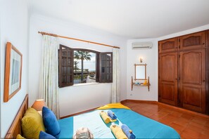 A room with a bed, a window with curtains, a wooden wardrobe, and a wall-mounted shelf. - Villa with heatable pool and BBQ in Albufeira (Albufeira)