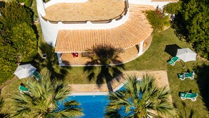 Une vue aérienne d’une maison avec une piscine, entourée de palmiers et d’un jardin.