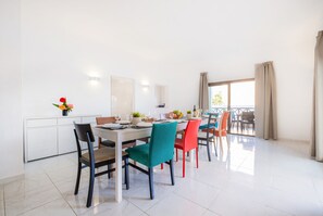 A dining area with a white table set for four, colorful chairs, and a view of the outdoors through a large window. - Comfort and fun with heatable pool and BBQ (Albufeira)