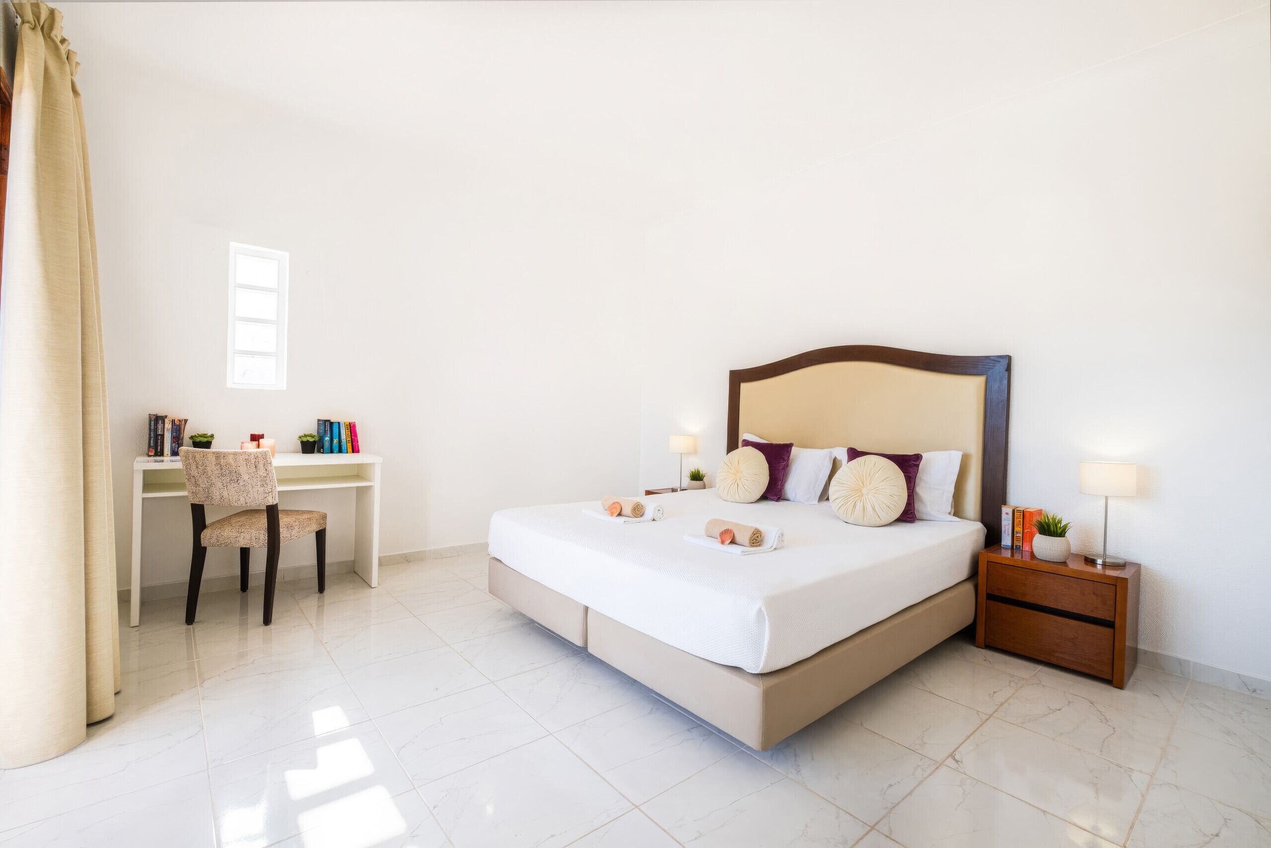 A hotel room with a bed, a desk, a chair, a nightstand, and a lamp.