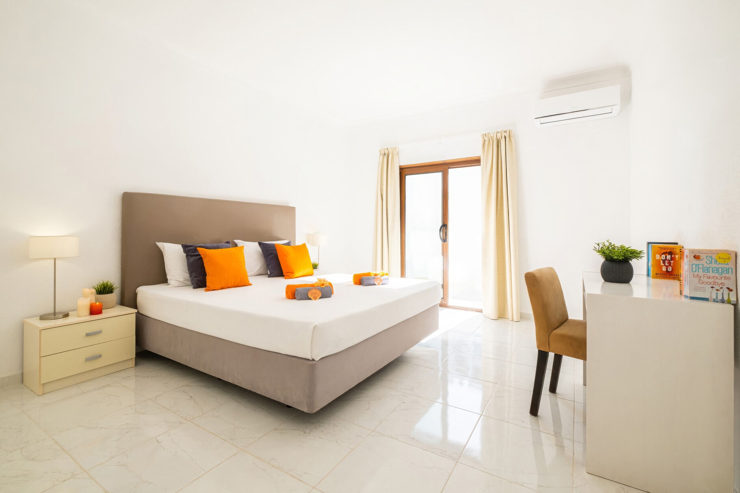 Quarto moderno com cama, mesa de cabeceira, abajur e escrivaninha com cadeira.
