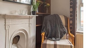 A room with a white fireplace, a wooden chair with a striped cushion, a large mirror, and a bookshelf with decorative items. - 4 Bed Town House - Reading Cent. (Reading)