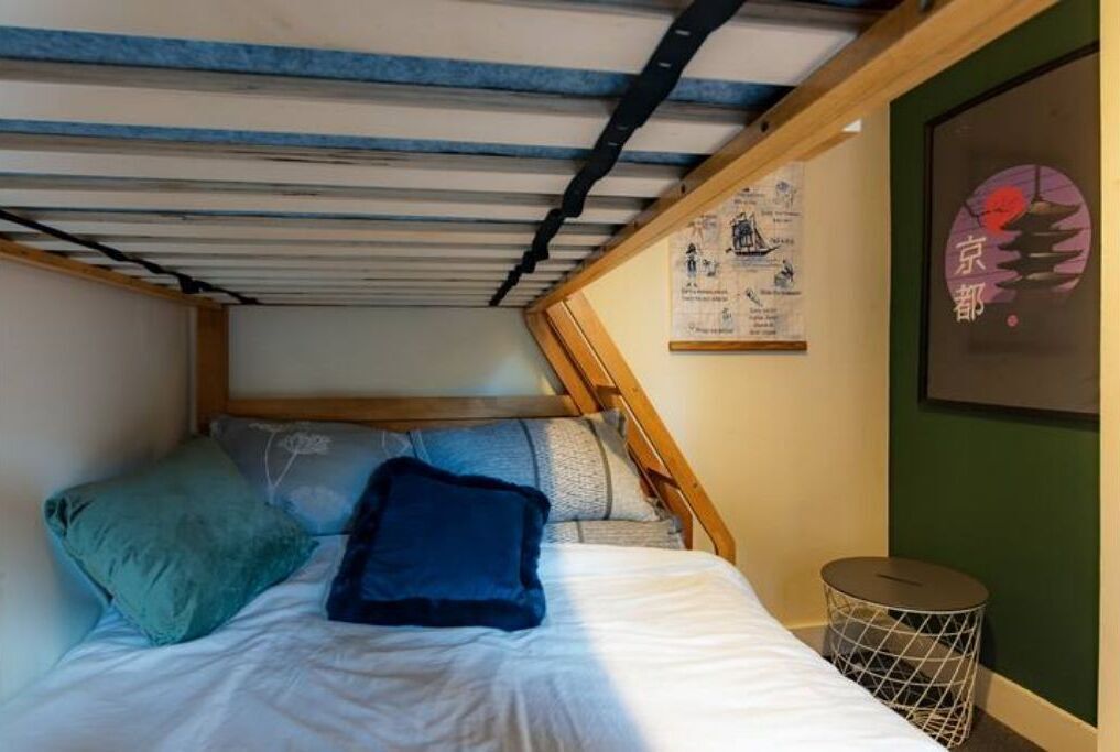 Un letto con testiera in legno, un cestino rotondo in metallo e un poster incorniciato appeso al muro.