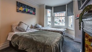 Une chambre avec deux lits, un lustre, un tableau et une vue sur la rue grâce à de grandes fenêtres.