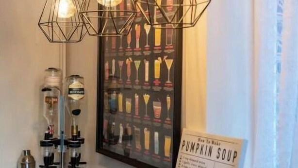 Une pièce avec un plancher en bois, un luminaire fixé au mur, une affiche de cocktails et un présentoir à menus.