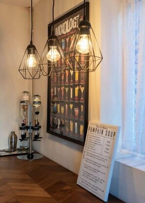 A room with a wooden floor, a wall-mounted light fixture, a poster of cocktails, and a menu stand. - Cozy Reading Cent. House 6 bed (Reading)