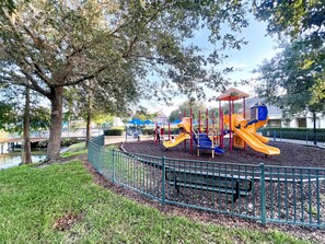 Un parque infantil con toboganes y estructuras de escalada, rodeado por una valla y árboles.
