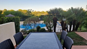 Un patio al aire libre con mesa y sillas, piscina y palmeras.