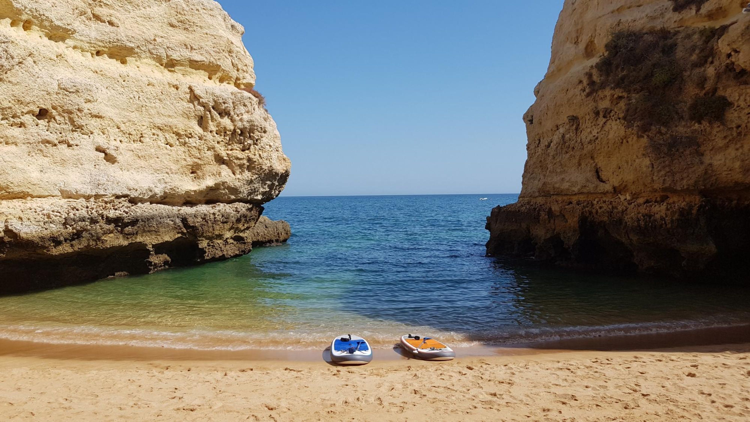 Una playa con dos barcos en la arena, mar azul cristalino y acantilados rocosos.