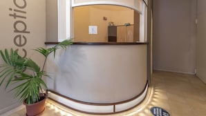 Un espace d’accueil avec un comptoir d’accueil incurvé, une plante en pot et un panneau sur le mur.