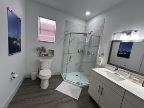 Un bagno moderno con cabina doccia in vetro, un water, un mobile lavabo con specchio e una finestra con persiane.