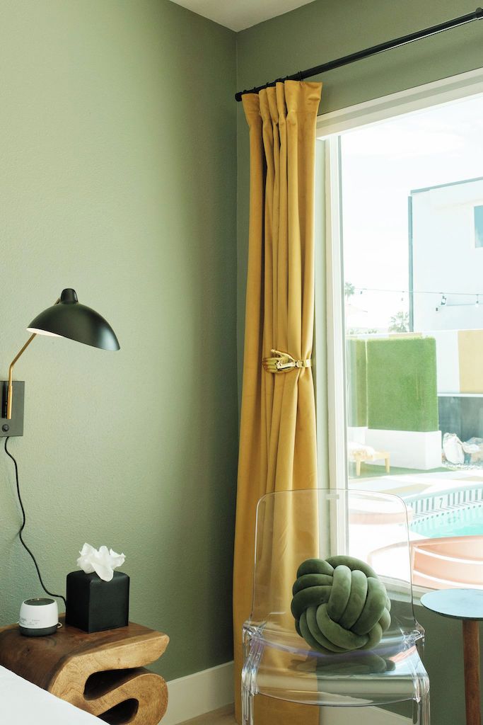 A room with a wooden side table, a black lamp, a tissue box, and a clear vase with a green object.