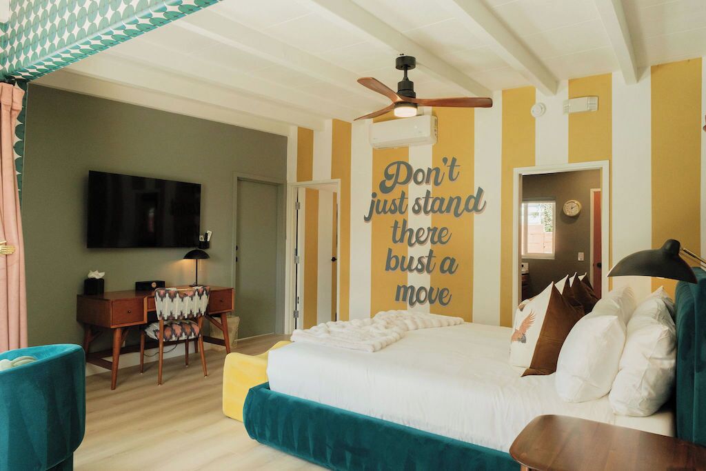 Un dormitorio con una cama, un escritorio, una silla, un televisor y una frase motivacional en la pared.