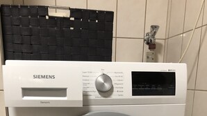 Een Siemens Sensoriq wasmachine met een digita bedieningspaneel, in een betegelde ruimte.