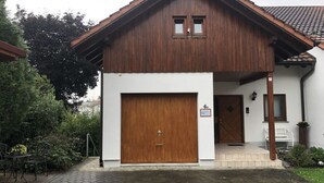 Een houten huis met twee verdiepingen, een grote garage deur, een klein portaaltje en een pannendak.