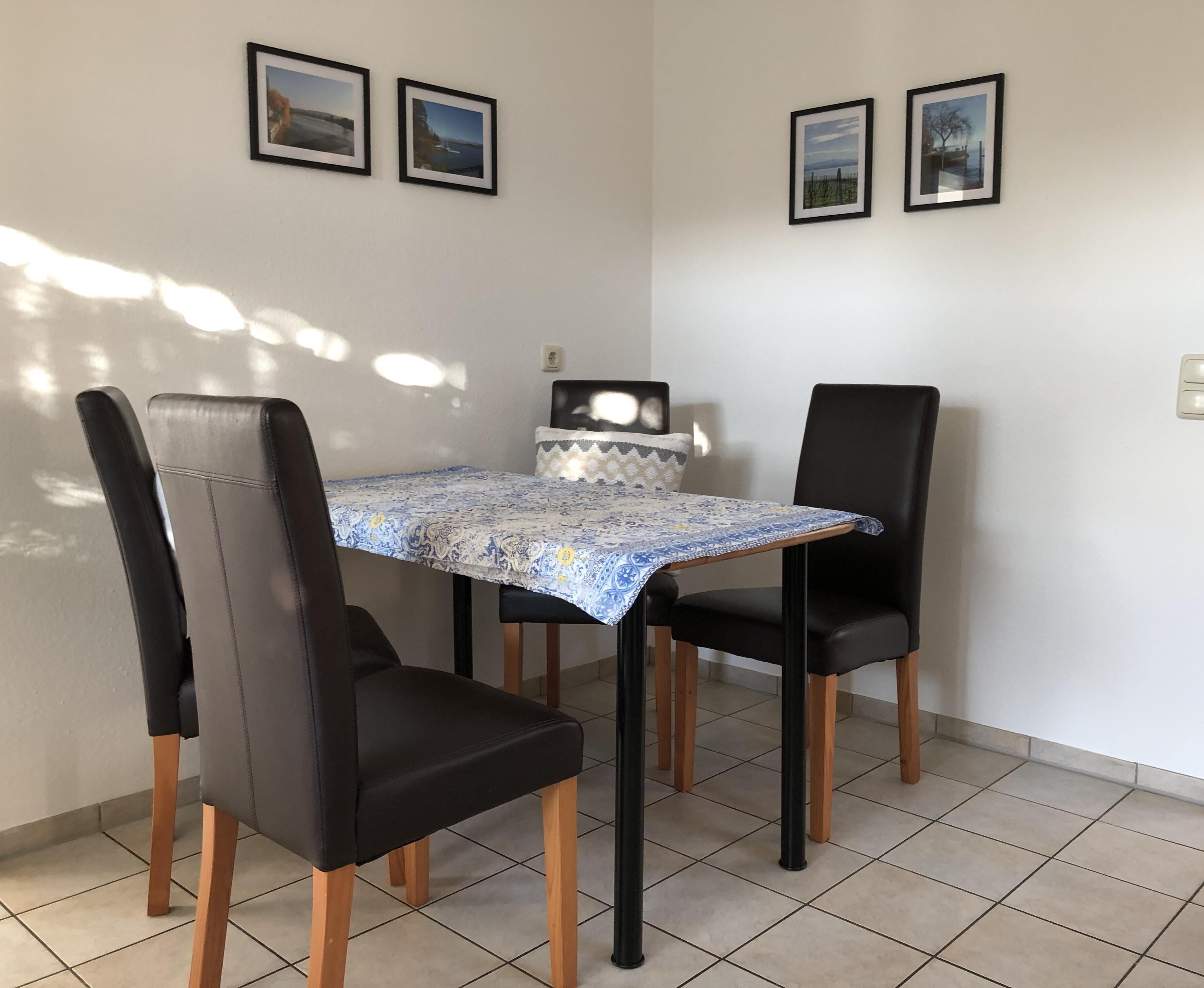 Zona pranzo con tavolo ricoperto da una tovaglia fantasia, quattro sedie nere e tre quadri appesi al muro.
