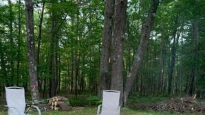 A campfire with two metal chairs and a fire pit surrounded by rocks. - Sutter Northwoods Home (Eagle River)
