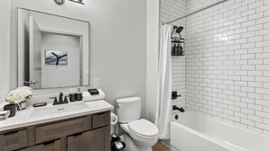 A modern bathroom with a white toilet, a vanity with a mirror, and a shower area with white tiles. - The Gatsby Getaway, Downtown LEX (Lexington)