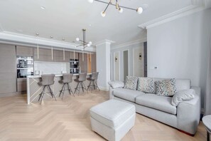 A modern living room with a grey sofa, matching ottoman, and a dining area with bar stools.