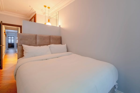 Un lit bien fait dans une chambre d’hôtel, avec une tête de lit, un couloir avec une porte et un luminaire au-dessus du lit.