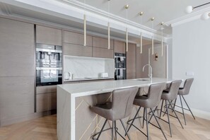 Una cocina moderna con encimera de mármol, electrodomésticos de acero inoxidable y una zona de bar con cuatro sillas.