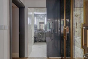 Un baño moderno con cabina de ducha de vidrio, azulejos de mármol y puerta de madera con pomo de latón.