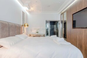 A modern hotel room with a large bed, a bedside table, a TV, and a walk-in closet. - Contemporarily Elegant 2BD Flat, Earl Court (London)