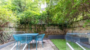 Eine Terrassengruppe mit Tisch und Stühlen, umgeben von Grünpflanzen und einer Ziegelwand.