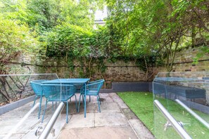 An outdoor patio with a table and chairs, surrounded by greenery and a brick wall.