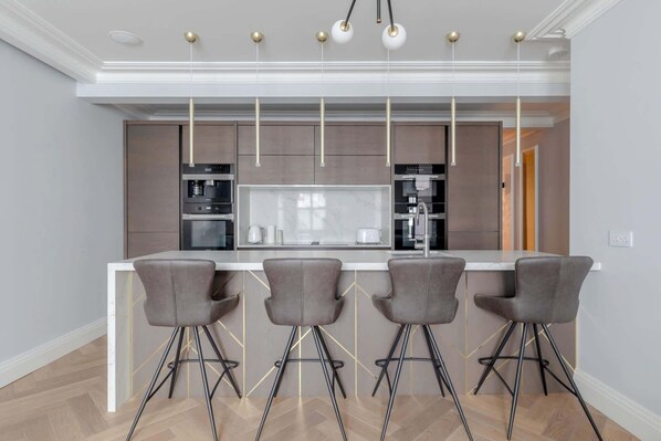 A modern kitchen with a central island, bar stools, and pendant lighting.