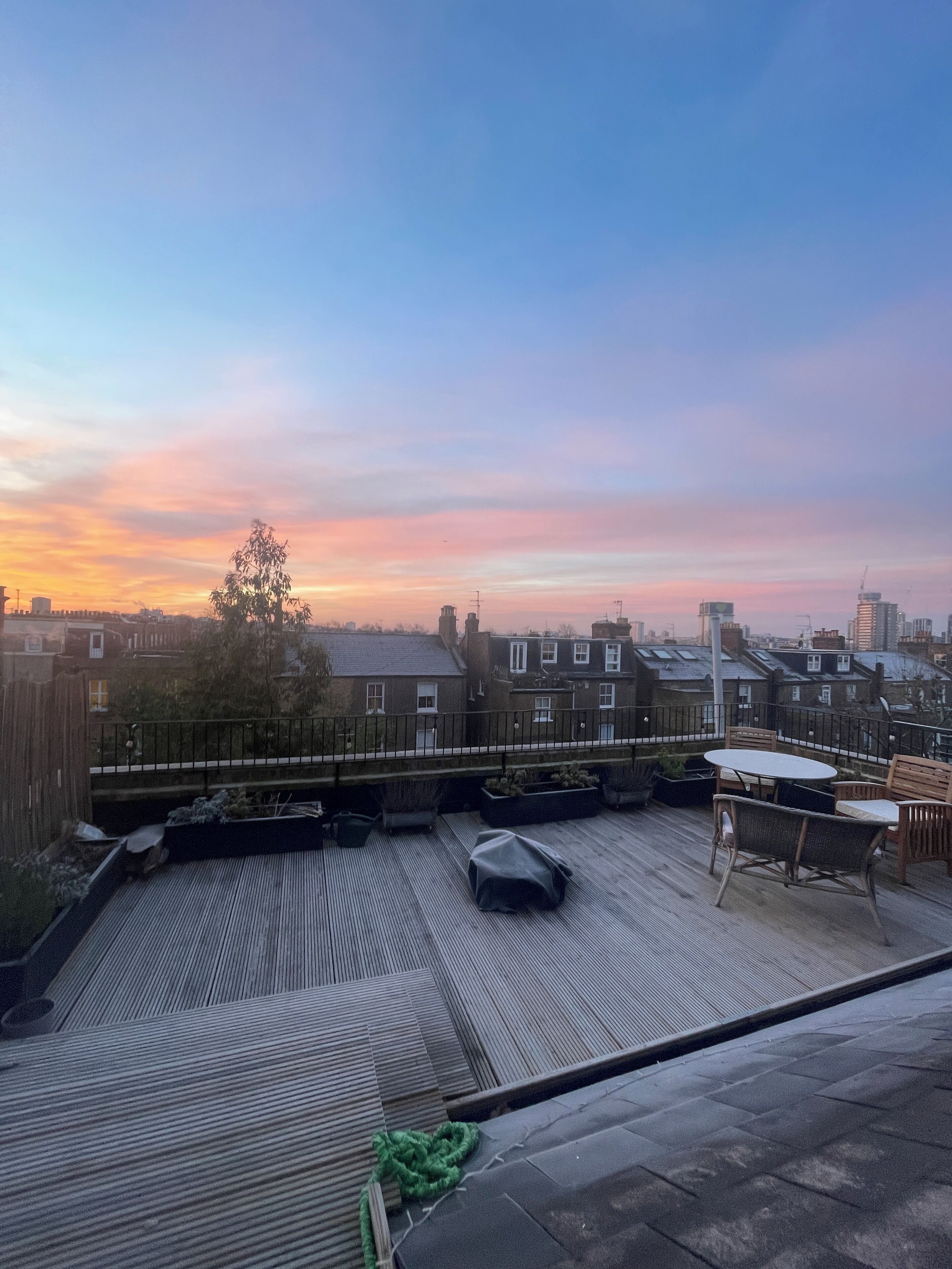 Een terras op het dak met uitzicht op een stadsgezicht tijdens de zonsondergang.