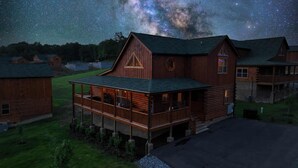 A rustic log cabin with a balcony, surrounded by other cabins, under a starry night sky.