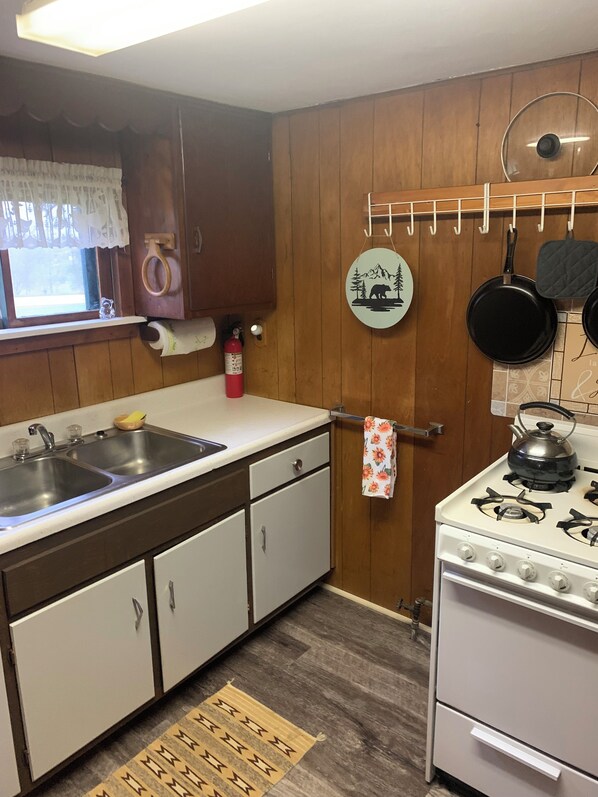 A kitchen with wooden cabinets, a white countertop, a stove, and a hanging pot rack. - Cozy, upgraded, pet friendly cabin, formerly Cuba Lake Vintage Duck House. (Cuba)