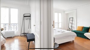 Une chambre lumineuse et spacieuse, avec un grand lit, un canapé vert et une étagère en métal noir.