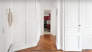 Un couloir avec des portes blanches, un plancher en bois et, au fond, on aperçoit une cuisine avec des meubles rouges.