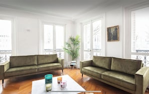A spacious living room with two green sofas, a white coffee table with candles, and large windows with shutters. - Magnificent apt in the heart of 16th Paris- 8 people. (Paris)