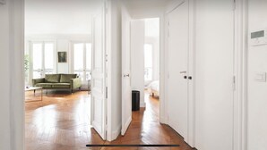 Un couloir avec des portes blanches qui donnent sur un salon où se trouve un canapé vert et un tableau au mur.