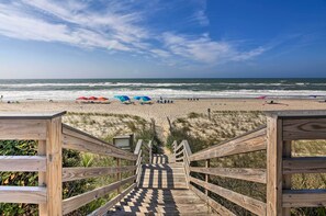 Una escalera de madera que conduce a una playa con sombrillas y sillas.