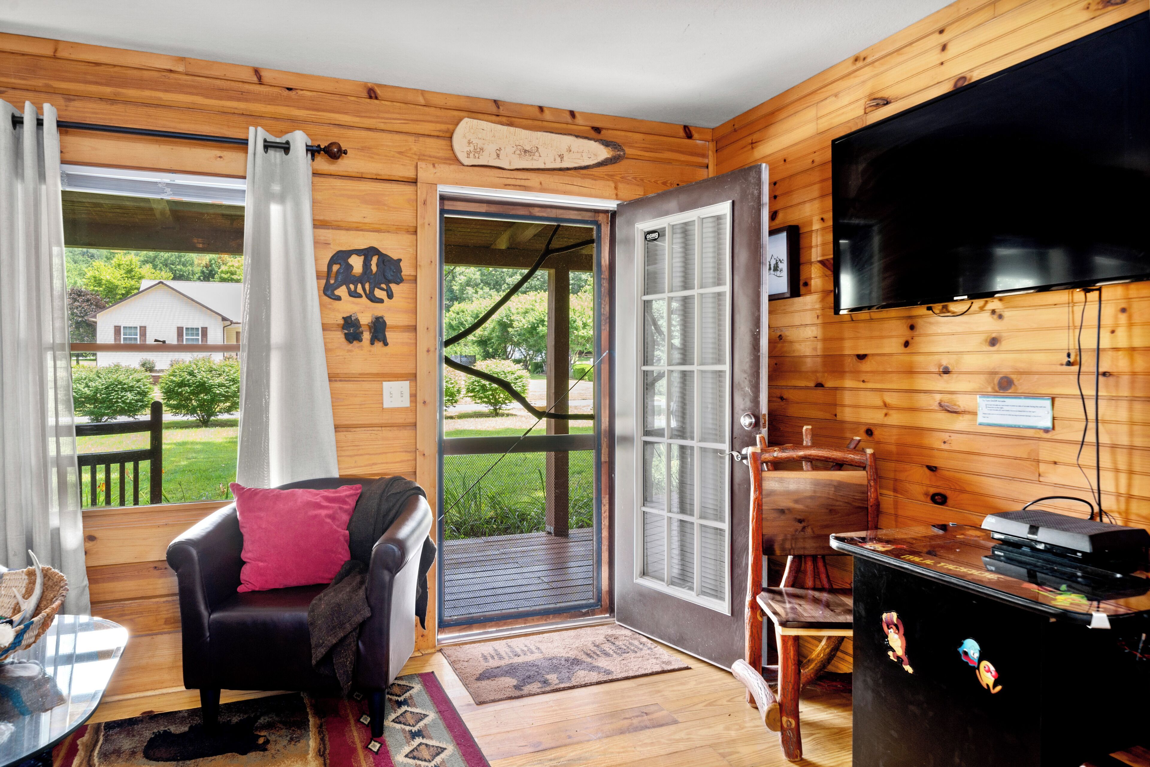 L’intérieur d’un chalet en bois est aménagé avec un canapé en cuir noir, un téléviseur et une porte qui donne sur une terrasse.