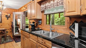A wooden cabin kitchen with a large window, wooden cabinets, a sink, and a stove. - Creekfront Cabin w/ Hot Tub! Motorcycle Friendly! (Robbinsville)