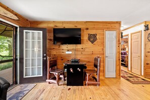 Een houten interieur met een aan de muur bevestigde televisie, een kleine tafel met stoelen en een deur die naar een andere kamer leidt.