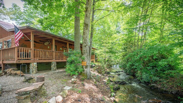 A cabin with a porch, surrounded by trees and a stream. - Creekfront Cabin w/ Hot Tub! Motorcycle Friendly! (Robbinsville)