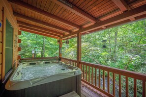 Een houten terras met een jacuzzi en uitzicht op een bos.