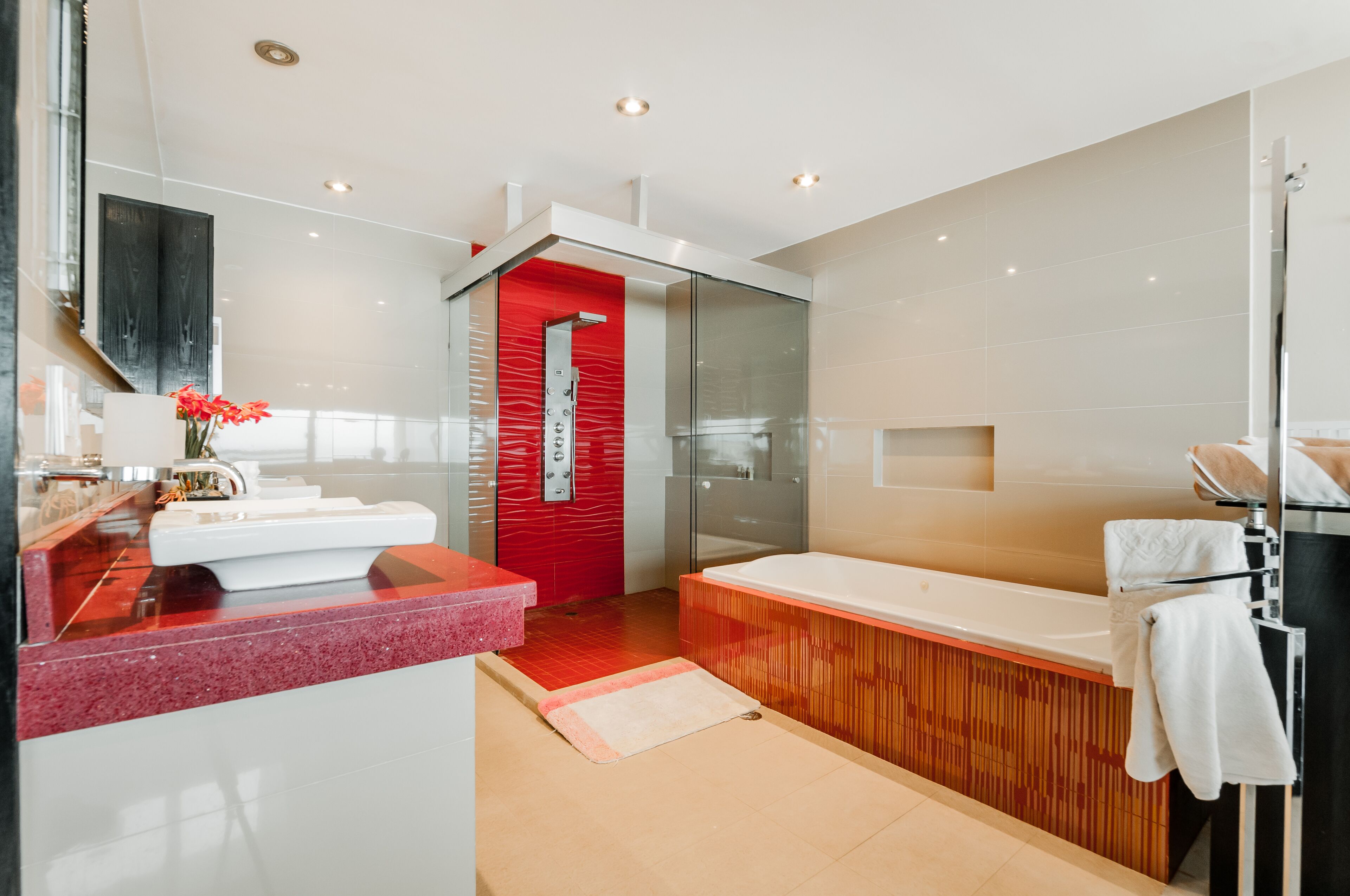 A modern bathroom with a glass shower enclosure, a large bathtub, and a vanity with a red countertop.
